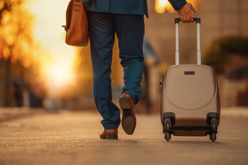 Rear of a man in a suit, pulling a wheely suitcase